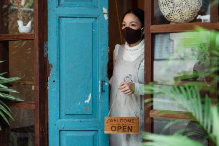 Mulher vestindo uma máscara na porta do seu comércio